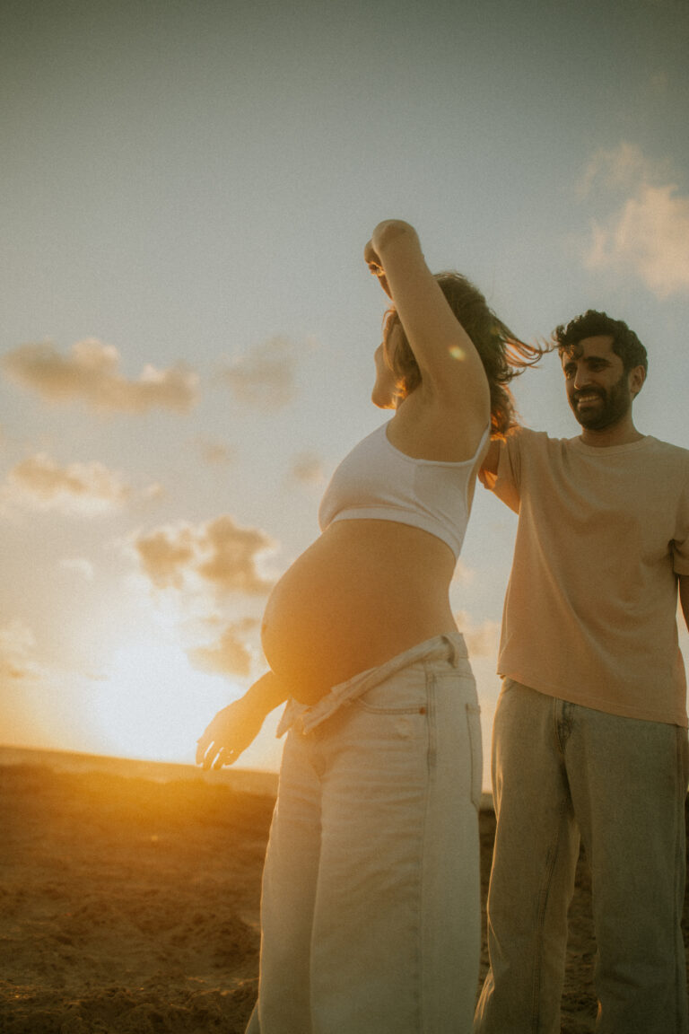 זוג בהריון בשקיעה, היא מרימה יד אל האור