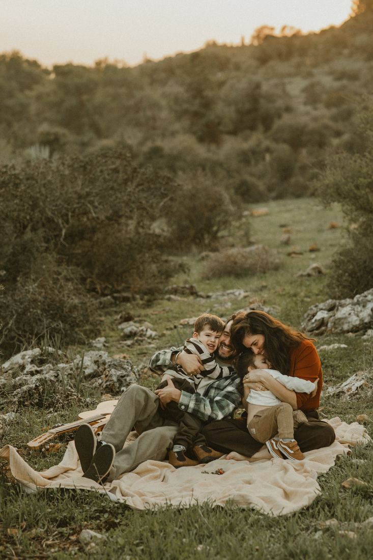 משפחה מתכרבלת על שמיכת פיקניק בטבע